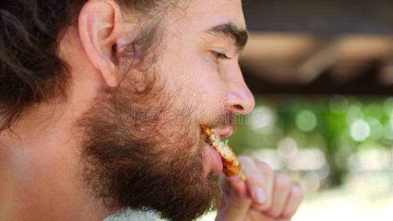 Um jovem com cadeado e barba come galinha