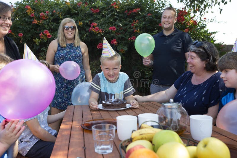 Um menino entusiasmado com a família em torno dele para comemorar um aniversário fotografia de stock Um menino entusiasmado com a família em torno dele para comemorar um aniversário fotografia de stock