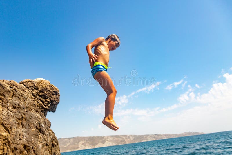 Um menino está saltando do penhasco no mar em um dia de verão quente Feriados na praia O conceito do turismo ativo fotos de stock royalty free Um menino está saltando do penhasco no mar em um dia de verão quente Feriados na praia O conceito do turismo ativo fotos de stock royalty free