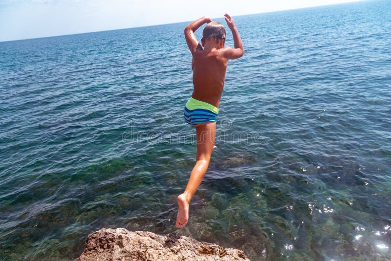 Um menino está saltando do penhasco no mar em um dia de verão quente Feriados na praia O conceito do turismo ativo foto de stock Um menino está saltando do penhasco no mar em um dia de verão quente Feriados na praia O conceito do turismo ativo foto de stock