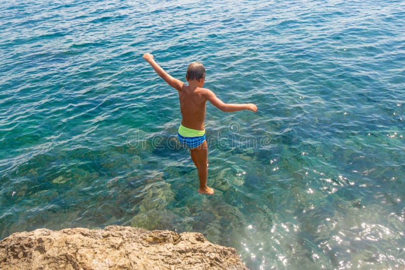 Um menino está saltando do penhasco no mar em um dia de verão quente Feriados na praia O conceito do turismo ativo fotografia de stock Um menino está saltando do penhasco no mar em um dia de verão quente Feriados na praia O conceito do turismo ativo fotografia de stock