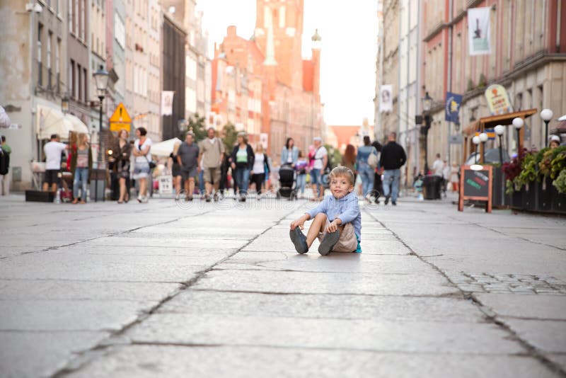 Um menino louro pequeno que senta-se em uma terra em um centro da cidade imagem de stock