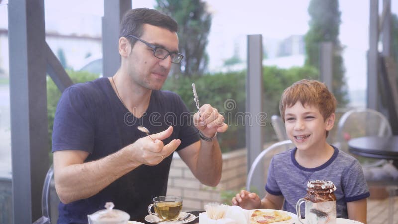 Um pai novo tenta seu cocktail do leite do ` s do filho com gelado e o chocolate, o filho ri, a família está jantando no