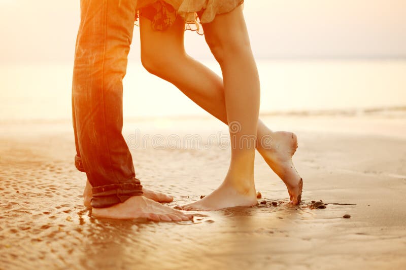 Um par novo loving que abraça e que beija na praia no por do sol imagens de stock royalty free Um par novo loving que abraça e que beija na praia no por do sol imagens de stock royalty free