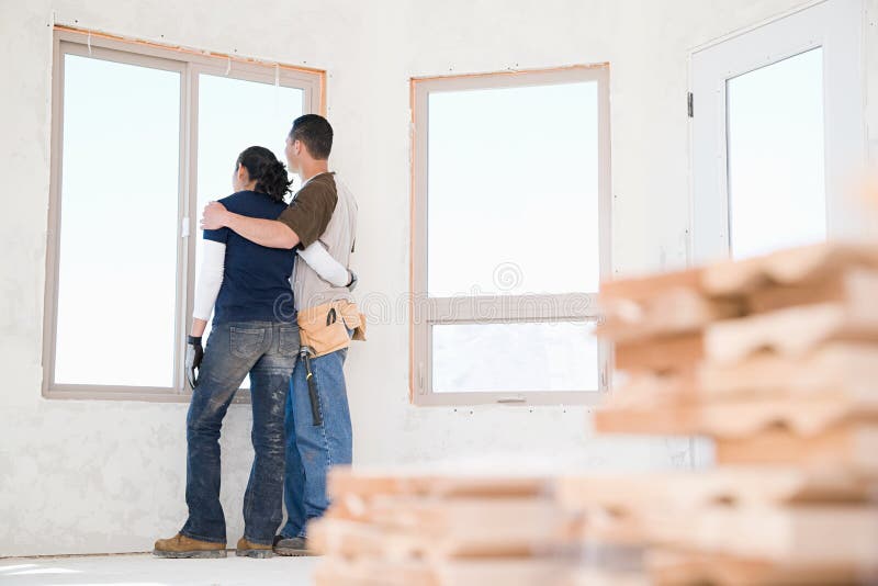 Um par que olha fora de uma janela de sua casa nova imagem de stock Um par que olha fora de uma janela de sua casa nova imagem de stock