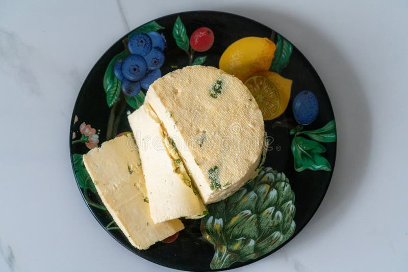 Um pedaço de queijo caseiro com endro e especiarias num prato preto imagens de stock royalty free