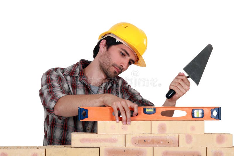 A mason using a level to check his wall. A mason using a level to check his wall.