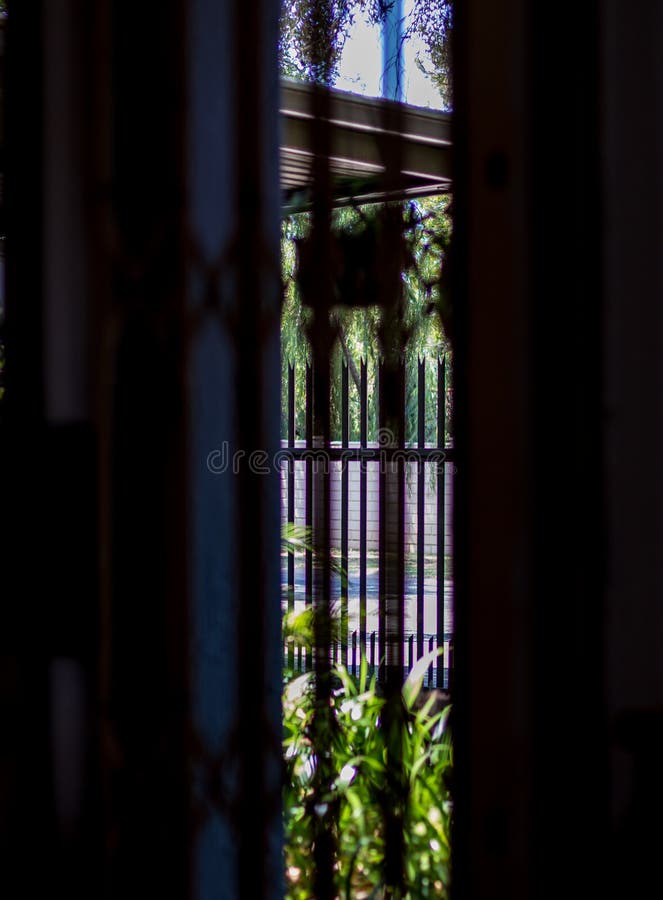 A glimpse of the outdoors through bars in a gap in a high wall image in portrait format. A glimpse of the outdoors through bars in a gap in a high wall image in portrait format