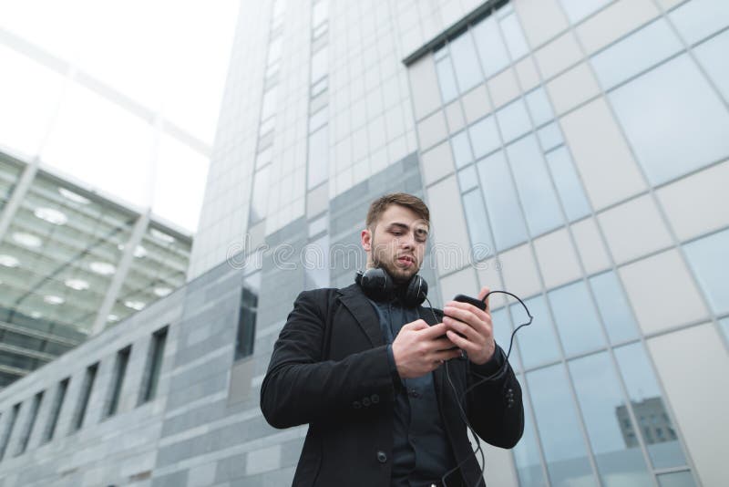 Um retrato da rua de um homem de negócios com uma barba que olhe seu smartphone, e está indo escutar a música imagens de stock Um retrato da rua de um homem de negócios com uma barba que olhe seu smartphone, e está indo escutar a música imagens de stock