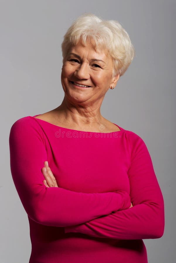 An old lady's portrait in pink casual clothes.On grey background. An old lady's portrait in pink casual clothes.On grey background.