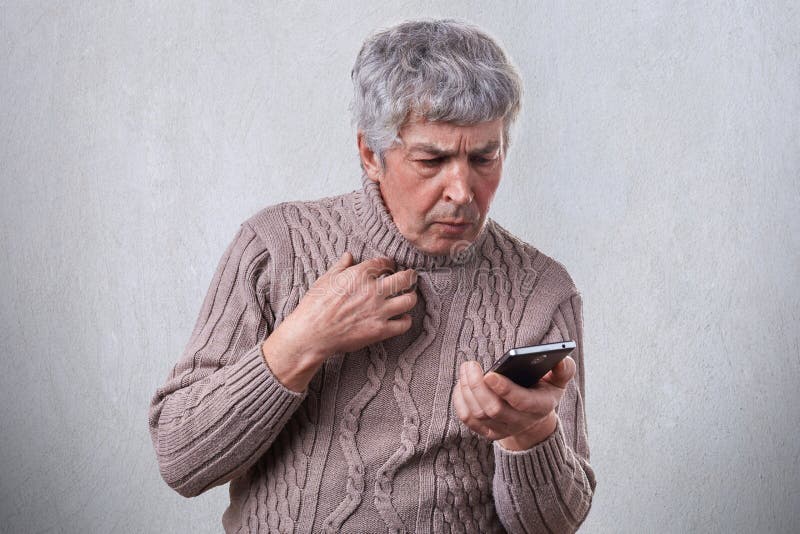 Um retrato do homem idoso com o cabelo cinzento que choca a expressão ao olhar em sua mensagem da leitura do smartphone Um looki imagens de stock Um retrato do homem idoso com o cabelo cinzento que choca a expressão ao olhar em sua mensagem da leitura do smartphone Um looki imagens de stock