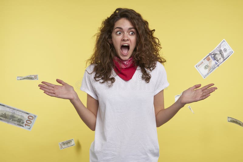 Um tiro do estúdio da mulher que ganha muito dinheiro, dinheiro que cai em sua cabeça, isolada sobre o fundo amarelo foto de stock Um tiro do estúdio da mulher que ganha muito dinheiro, dinheiro que cai em sua cabeça, isolada sobre o fundo amarelo foto de stock