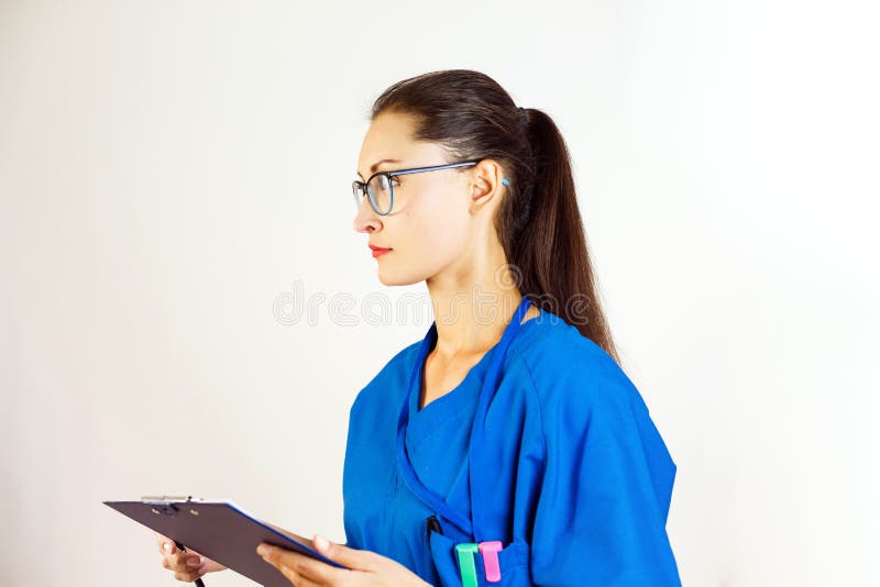 Um trabalhador médico fêmea guarda um dobrador em suas mãos e olhares à esquerda, está vestindo vidros e um uniforme azul branco fotos de stock royalty free Um trabalhador médico fêmea guarda um dobrador em suas mãos e olhares à esquerda, está vestindo vidros e um uniforme azul branco fotos de stock royalty free