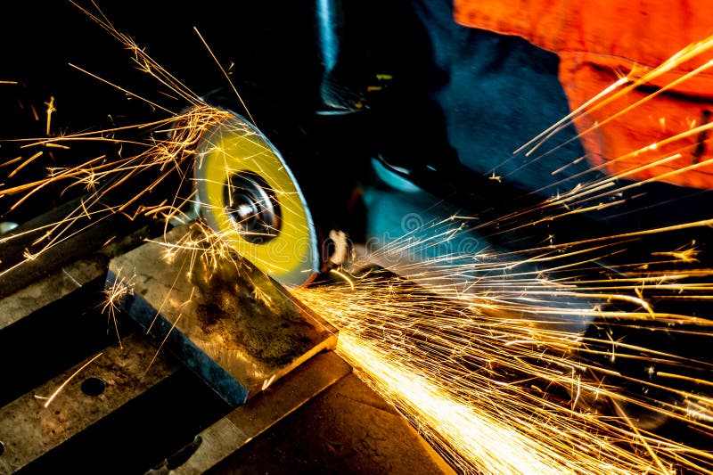 Um trabalhador vê uma placa do metal com uma roda de corte com uma máquina de moedura, grandes faíscas voa ao redor fotografia de stock royalty free Um trabalhador vê uma placa do metal com uma roda de corte com uma máquina de moedura, grandes faíscas voa ao redor fotografia de stock royalty free