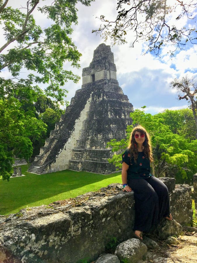 Um turista fêmea novo bonito que levanta na frente das ruínas de Tikal fotografia de stock Um turista fêmea novo bonito que levanta na frente das ruínas de Tikal fotografia de stock