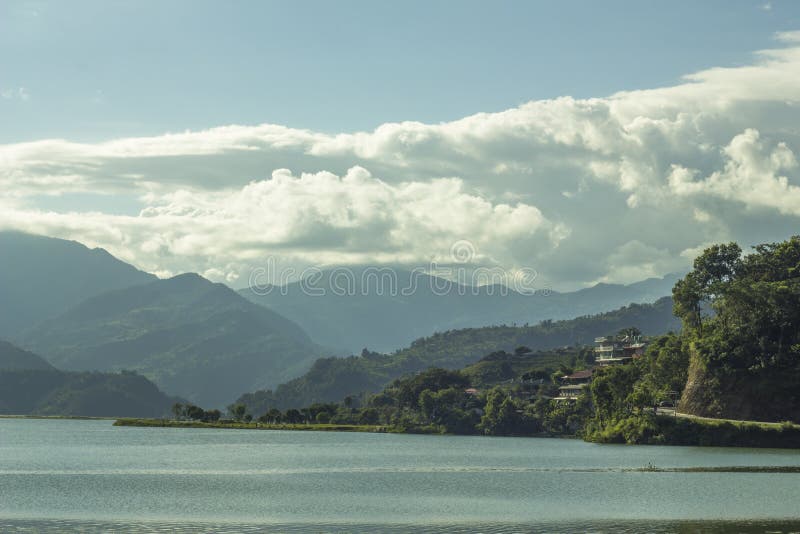 Um vale verde da montanha sob um céu azul com nuvens e as casas brancas contra um lago foto de stock royalty free Um vale verde da montanha sob um céu azul com nuvens e as casas brancas contra um lago foto de stock royalty free