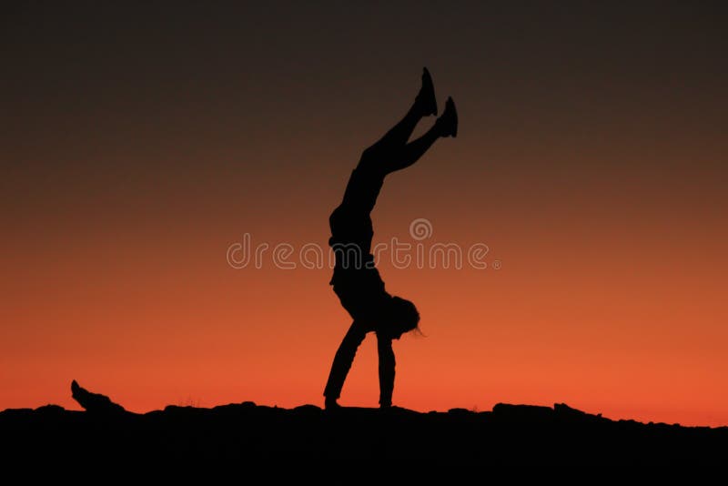 Um viajante masculino novo está em suas mãos e executa figuras acrobáticas em um fundo do vermelho brilhante com o céu alaranjado foto de stock royalty free Um viajante masculino novo está em suas mãos e executa figuras acrobáticas em um fundo do vermelho brilhante com o céu alaranjado foto de stock royalty free