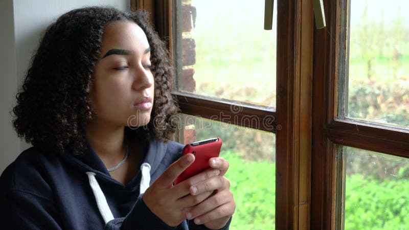 Uma adolescente afro-americana triste ou deprimida, de raça mista, usando seu celular para redes sociais
