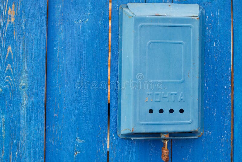 Uma caixa postal sovi?tica azul velha com uma inscri??o e um fechamento oxidado que penduram em uma cerca azul de madeira rural imagem de stock Uma caixa postal sovi?tica azul velha com uma inscri??o e um fechamento oxidado que penduram em uma cerca azul de madeira rural imagem de stock