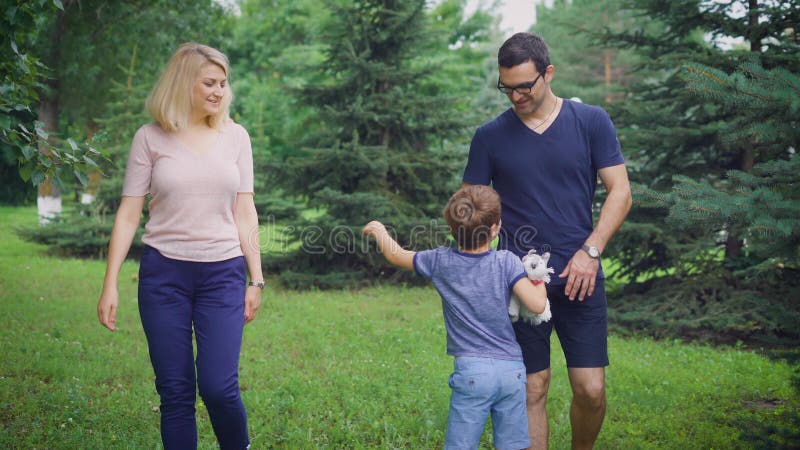 Uma caminhada nova da família através do parque no verão, o pai toma seu filho em seus braços, a mãe agrada o menino