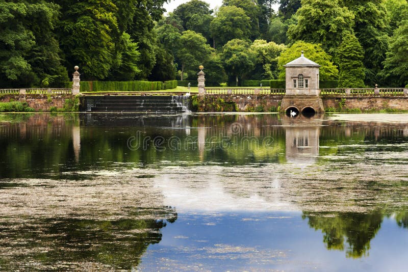 A swan swims in the reflections on the pond at this stately home located near Fountains Abbey in Studley Park, Ripon, Yorkshire England. The manor house is open to the public and the grounds are beautifully maintained. The trees surround this pond and the swans cast a reflection in the still waters. This image might bring to mind a princess and her palace or maybe one might think of Swan Lake by Tchaikovsky. Either way, this photo is full of magic, mood, and romance. A swan swims in the reflections on the pond at this stately home located near Fountains Abbey in Studley Park, Ripon, Yorkshire England. The manor house is open to the public and the grounds are beautifully maintained. The trees surround this pond and the swans cast a reflection in the still waters. This image might bring to mind a princess and her palace or maybe one might think of Swan Lake by Tchaikovsky. Either way, this photo is full of magic, mood, and romance