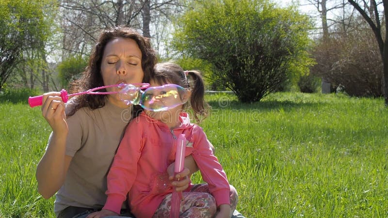 Uma criança com sua mãe está jogando com bolhas de sabão Uma família feliz no selvagem A mamã e a filha estão fundindo bolhas