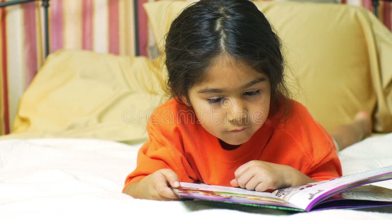 Uma criança latino-americano pequena bonito que encontra-se na cama que lê quietamente