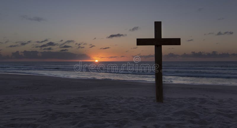 Uma cruz velha na duna de areia ao lado do oceano com um nascer do sol calmo foto de stock Uma cruz velha na duna de areia ao lado do oceano com um nascer do sol calmo foto de stock