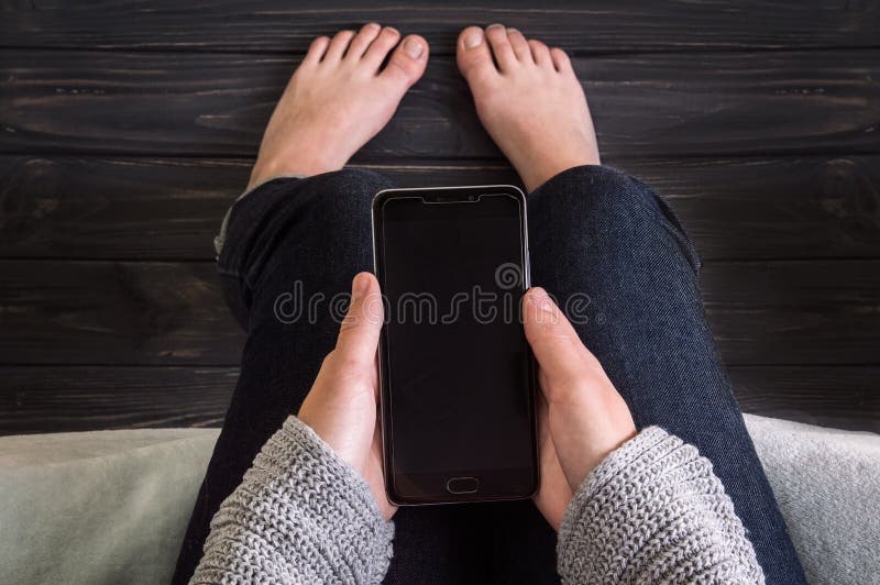 Uma determinada menina senta e guarda um smartphone preto em suas mãos Fundo escuro do passeio à beira mar fotografia de stock Uma determinada menina senta e guarda um smartphone preto em suas mãos Fundo escuro do passeio à beira mar fotografia de stock