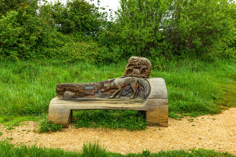 Uma escultura do banco da relembrança ao longo de um trajeto com vegetação e as árvores verdes fotos de stock Uma escultura do banco da relembrança ao longo de um trajeto com vegetação e as árvores verdes fotos de stock