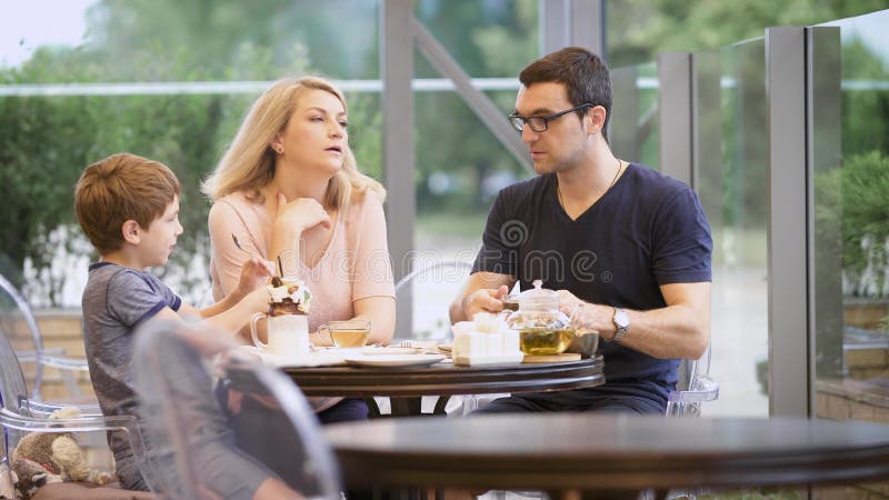 Uma família ordinária janta em um restaurante, o chá quente das bebidas do pai, o filho é ocupado com um milk shake com chocolate