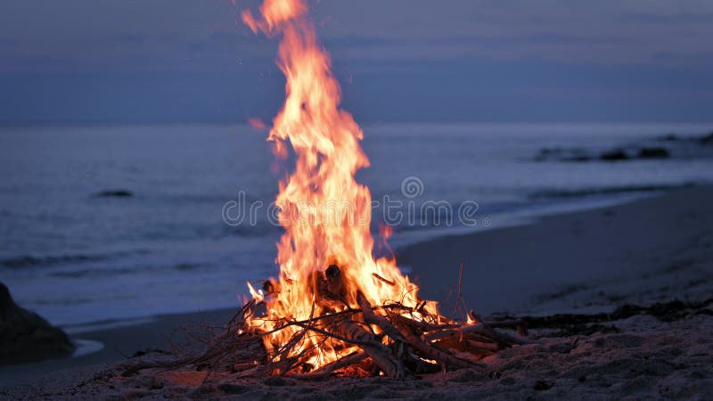 Uma fogueira queima em uma praia deserta de arenito na costa da noite