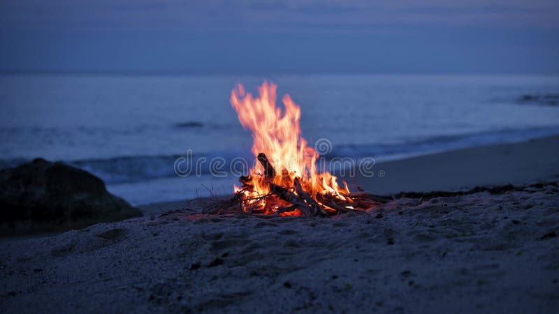 Uma fogueira queima em uma praia deserta de arenito na costa da noite