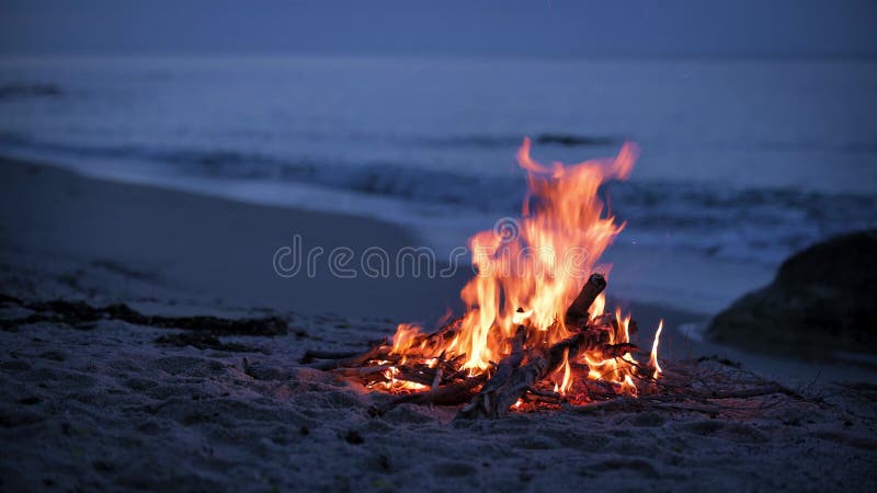 Uma fogueira queima em uma praia deserta de arenito na costa da noite