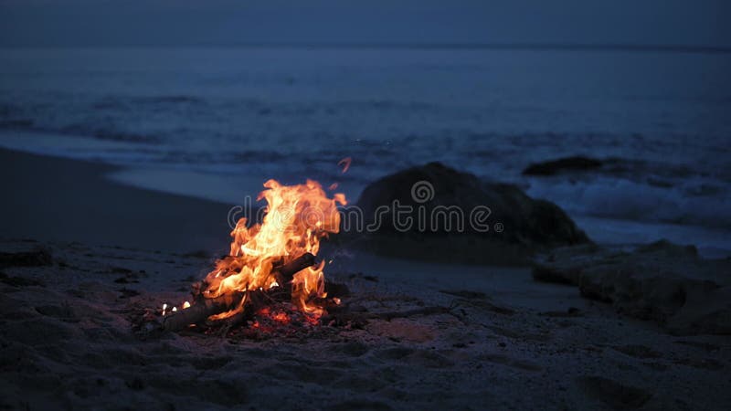 Uma fogueira queima em uma praia deserta de arenito na costa da noite