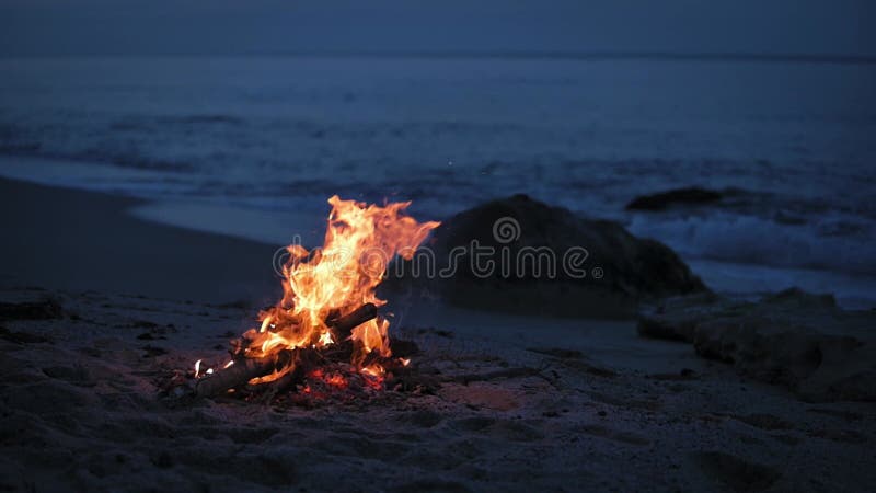 Uma fogueira queima em uma praia deserta de arenito na costa da noite