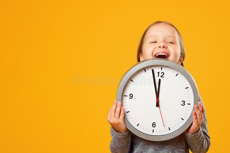 Uma garotinha olha de baixo do relógio Fundo amarelo O conceito de educação, escola, tempo de aprender fotos de stock Uma garotinha olha de baixo do relógio Fundo amarelo O conceito de educação, escola, tempo de aprender fotos de stock