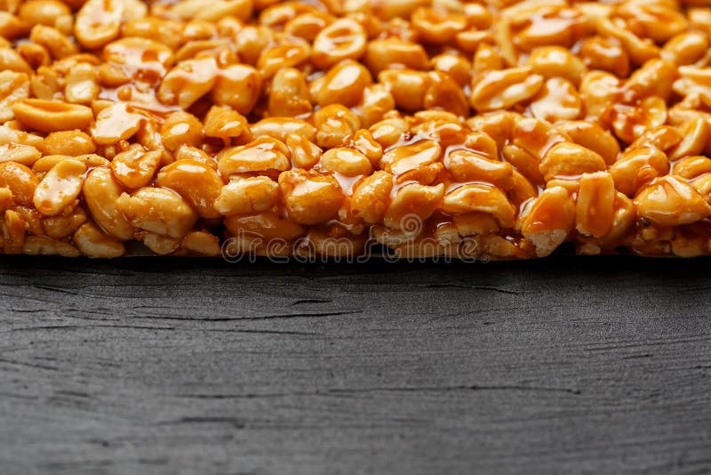 Uma grande telha dourada dos amendoins, uma barra em um melaço doce em um fundo preto da textura Doces úteis e saborosos de Kozin imagens de stock Uma grande telha dourada dos amendoins, uma barra em um melaço doce em um fundo preto da textura Doces úteis e saborosos de Kozin imagens de stock
