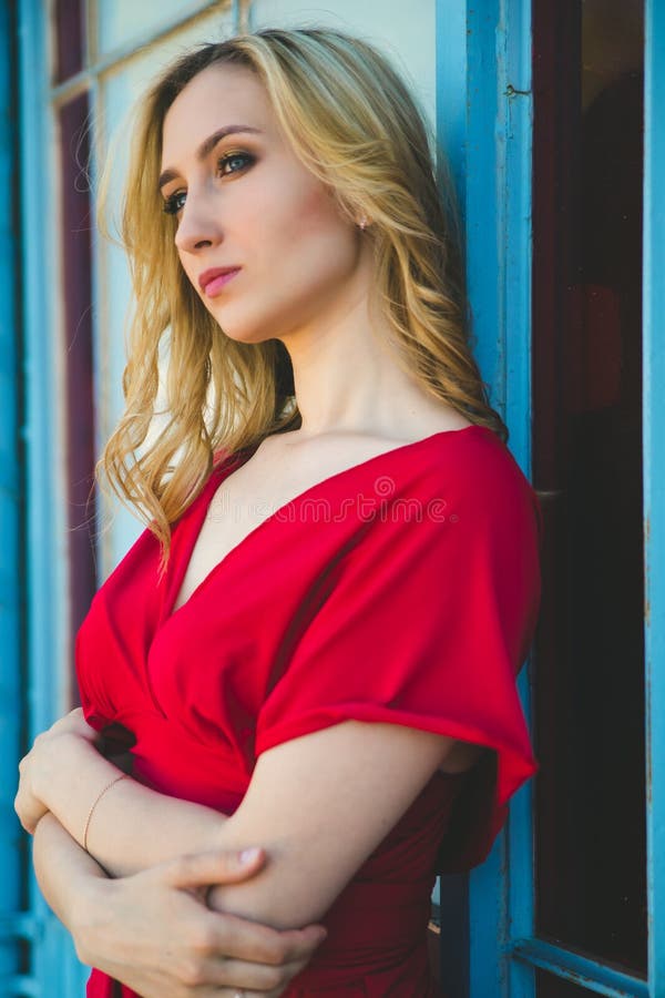 A young woman stands in front of a beautiful old building. A girl in an elegant red dress. Femininity and beauty.The girl leaned back against the wall.A thoughtful look. A young woman stands in front of a beautiful old building. A girl in an elegant red dress. Femininity and beauty.The girl leaned back against the wall.A thoughtful look