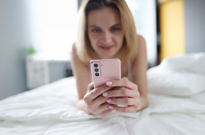 Beautiful blonde lies on the bed with a smartphone, close-up, blurry. Woman 30 years old reads online, internet in a hotel. Beautiful blonde lies on the bed with a smartphone, close-up, blurry. Woman 30 years old reads online, internet in a hotel