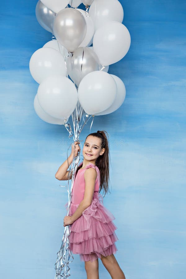 Uma menina adolescente bonita com cabelo marrom em um vestido cor-de-rosa que guarda muitos balões imagem de stock royalty free Uma menina adolescente bonita com cabelo marrom em um vestido cor-de-rosa que guarda muitos balões imagem de stock royalty free