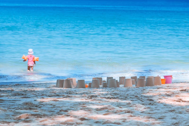 Uma menina anda na água para nadar Feito muitas figuras da areia na praia Férias com as crianças pelo mar Adultos novos fotos de stock Uma menina anda na água para nadar Feito muitas figuras da areia na praia Férias com as crianças pelo mar Adultos novos fotos de stock