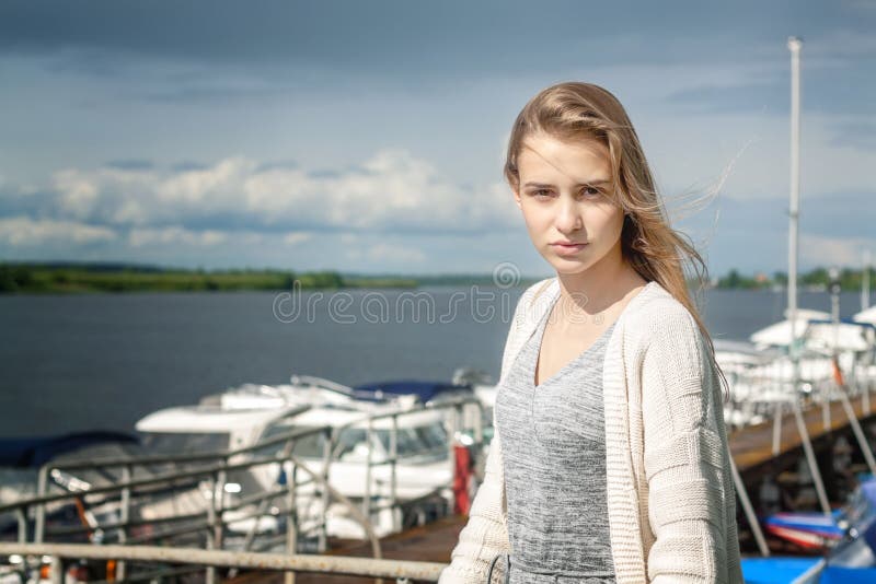 Uma menina bonita está sozinha no cais na perspectiva da superfície e dos nuvems tempestuosa aquosos que estendem além do hori imagem de stock royalty free Uma menina bonita está sozinha no cais na perspectiva da superfície e dos nuvems tempestuosa aquosos que estendem além do hori imagem de stock royalty free