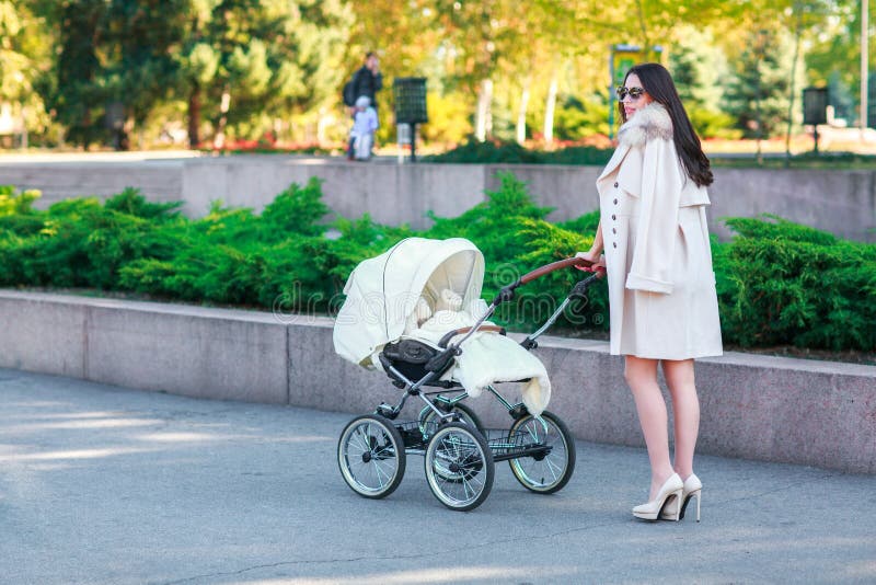 Uma menina com cabelo longo escuro anda com um bebê no parque imagem de stock Uma menina com cabelo longo escuro anda com um bebê no parque imagem de stock