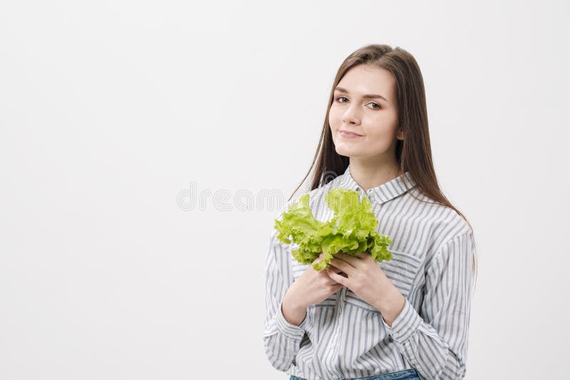Uma menina moreno delgada com cabelo longo em um fundo branco, realiza em suas mãos e mostra as folhas de fresco verde imagem de stock royalty free Uma menina moreno delgada com cabelo longo em um fundo branco, realiza em suas mãos e mostra as folhas de fresco verde imagem de stock royalty free
