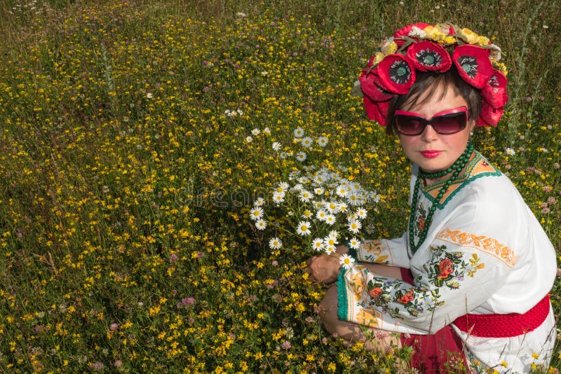 Uma menina no bordado ucraniano com uma grinalda em sua cabeça pelo lago em um prado entre as flores imagens de stock Uma menina no bordado ucraniano com uma grinalda em sua cabeça pelo lago em um prado entre as flores imagens de stock