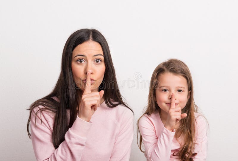 Uma menina pequena e sua mãe em um estúdio com um dedo em seus bordos fotos de stock Uma menina pequena e sua mãe em um estúdio com um dedo em seus bordos fotos de stock