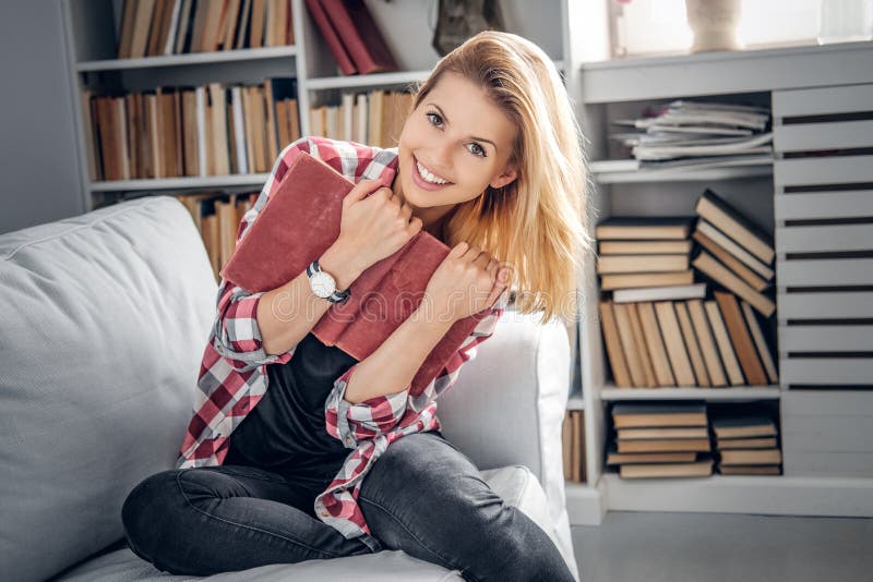Uma menina senta-se em um sofá e lê-se um livro em uma sala de visitas imagens de stock Uma menina senta-se em um sofá e lê-se um livro em uma sala de visitas imagens de stock