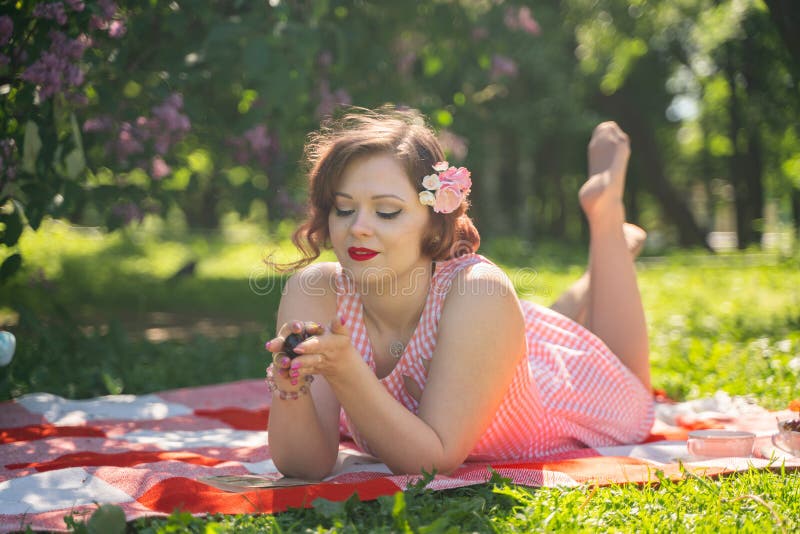 A charming pin up vintage retro young girl enjoys a rest and a picnic on the green summer grass alone. pretty woman have a holiday and spend vacantions on the nature. alone happy. A charming pin up vintage retro young girl enjoys a rest and a picnic on the green summer grass alone. pretty woman have a holiday and spend vacantions on the nature. alone happy