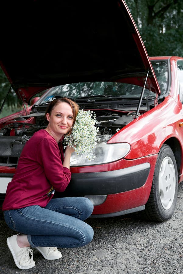 Uma moça está perto de um carro quebrado e dá-lhe flores imagem de stock Uma moça está perto de um carro quebrado e dá-lhe flores imagem de stock